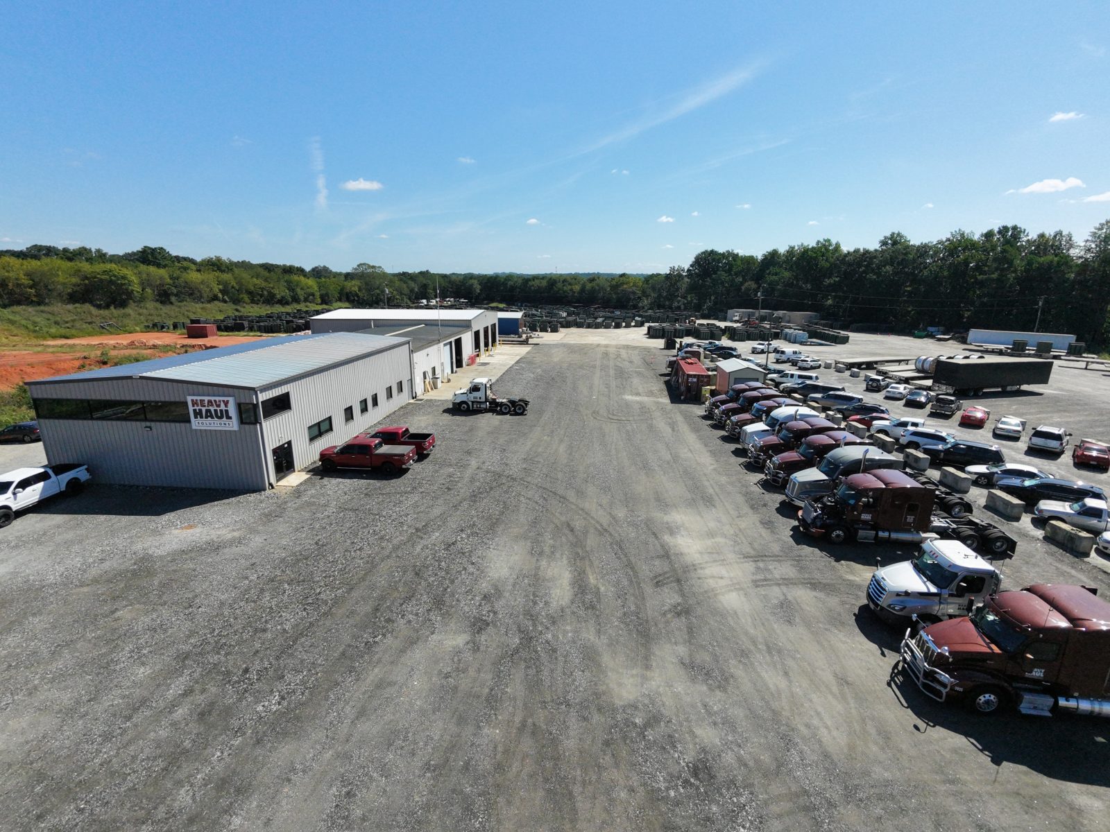 Aerial view of the Heavy Haul Solutions yard in Spartanburg, South Carolina: the office and shop building with a row of tractors parked along the gravel lot