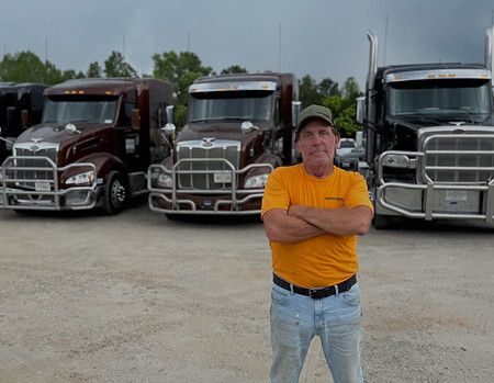 Heavy Haul Solutions CDL truck driver standing in front of company semi truck fleet