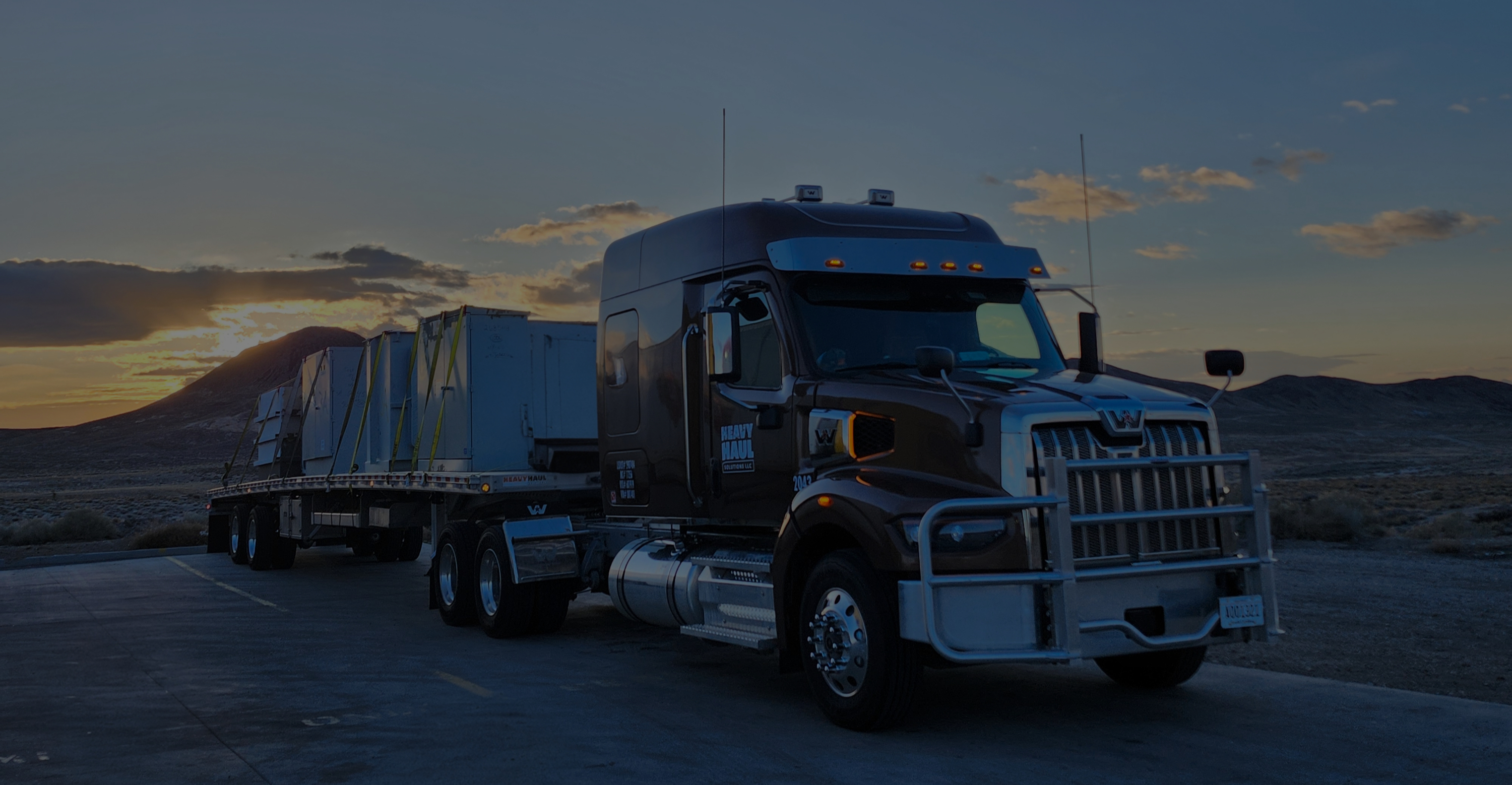 Blue flatbed semi truck parked at sunset in a desert landscape