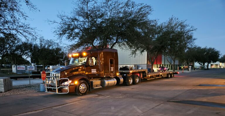Heavy Haul Solutions semi tractor with parked at a facility with stepdeck trailer, lit by evening light with trees in background.