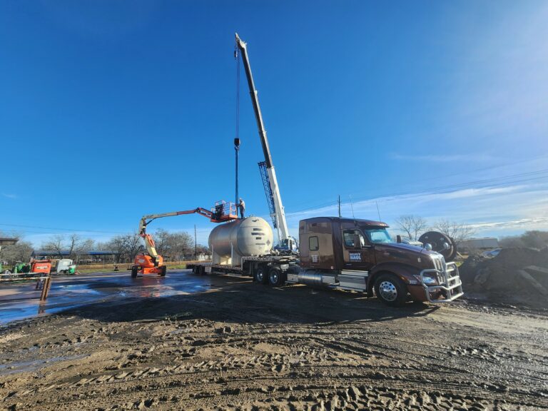Semi truck hauling a tank with crane and tank trailer parked at job site with equipment and vehicles nearby