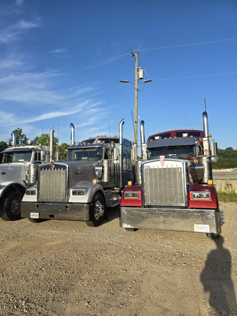 Three semi tractors parked side-by-side on gravel with utility pole and clear blue sky in background.