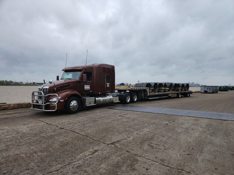 Semi tractor with stepdeck trailer carrying large industrial spools parked at a yard under cloudy skies