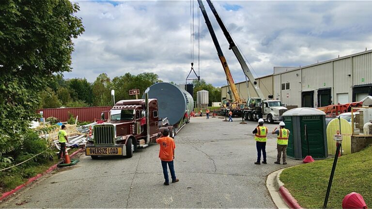 Tanker trailer parked at industrial facility with crane and workers in safety gear nearby.