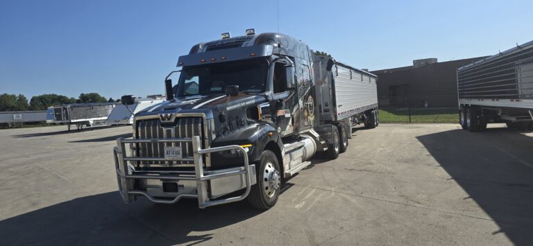 Semi tractor with enclosed trailer parked at industrial yard with other trailers visible in background.