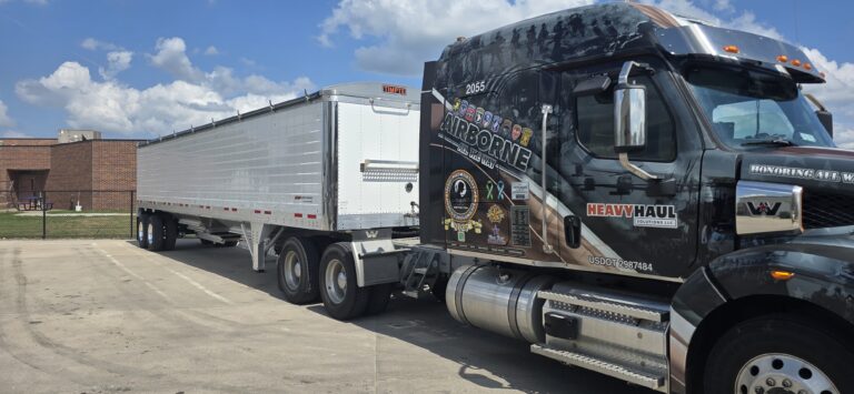 Heavy Haul Solutions semi tractor with step deck trailer parked at facility with brick building in background.