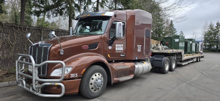 Heavy Haul Solutions semi tractor with flatbed trailer and lowboy parked at yard with equipment containers visible in background.