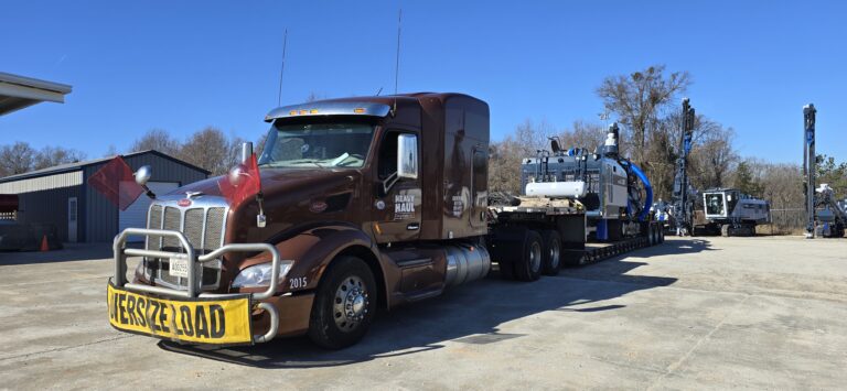 Heavy Haul Solutions semi tractor with oversized load permit parked at terminal lot with other equipment visible in background.