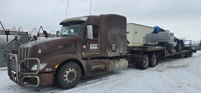 Heavy Haul Solutions semi tractor with step deck trailer carrying large boom parked in a snowy yard