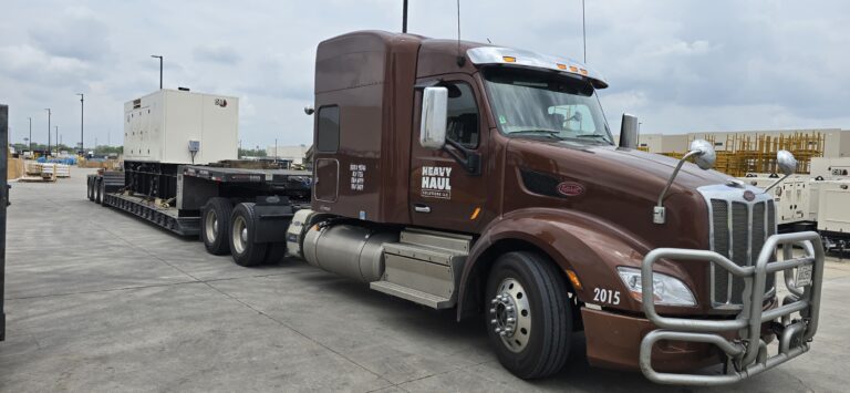 Semi tractor with RGN trailer parked in industrial yard, Heavy Haul Solutions branding visible on cab.