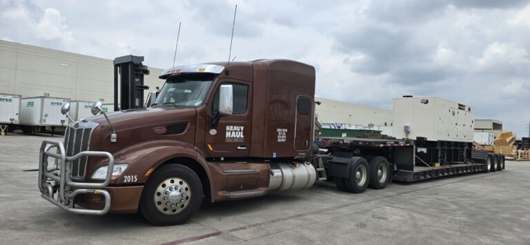 Heavy Haul Solutions semi tractor with step deck trailer parked in yard with industrial buildings and equipment visible in background.