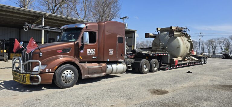 Heavy Haul Solutions semi tractor with brown cab parked at yard, pulling an RGN trailer