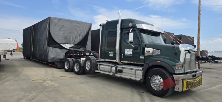 Semi tractor with RGN trailer carrying large black industrial modular unit