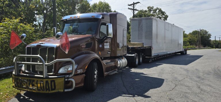 Semi tractor with enclosed trailer parked on paved lot, trees in background.