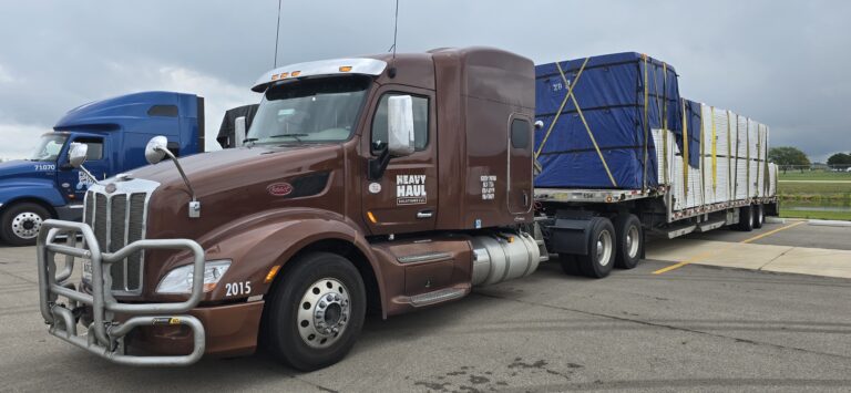 Semi tractor with Heavy Haul Solutions branding parked with livestock trailer; additional trucks visible in background.