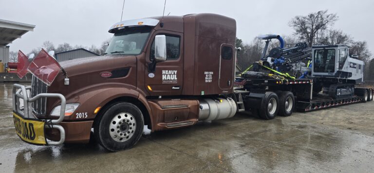 Heavy Haul Solutions semi tractor with RGN trailer parked at yard, carrying blue machinery on the deck