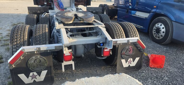 Lowboy trailer with red warning lights and Heavy Haul Solutions branding parked at facility with trucks visible in background.