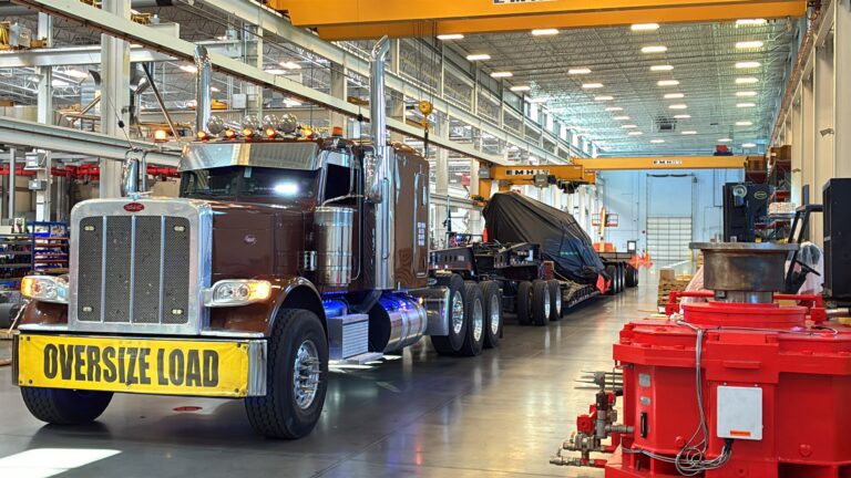 Semi tractor with oversize load banner parked in warehouse facility hauling a specialized trailer with equipment