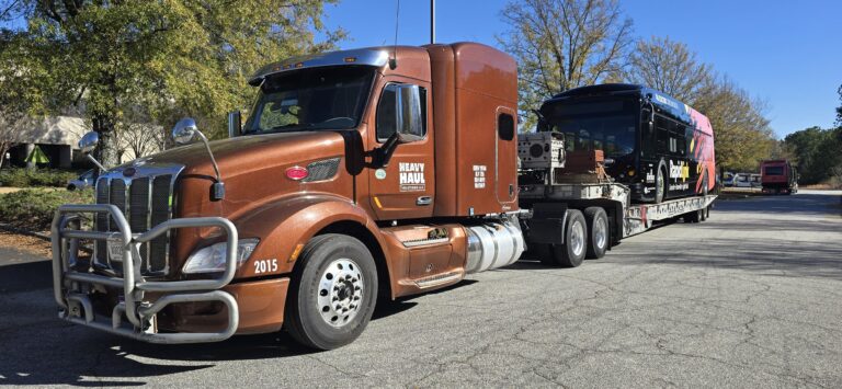 Semi tractor with brown cab towing a bus on a landoll trailer