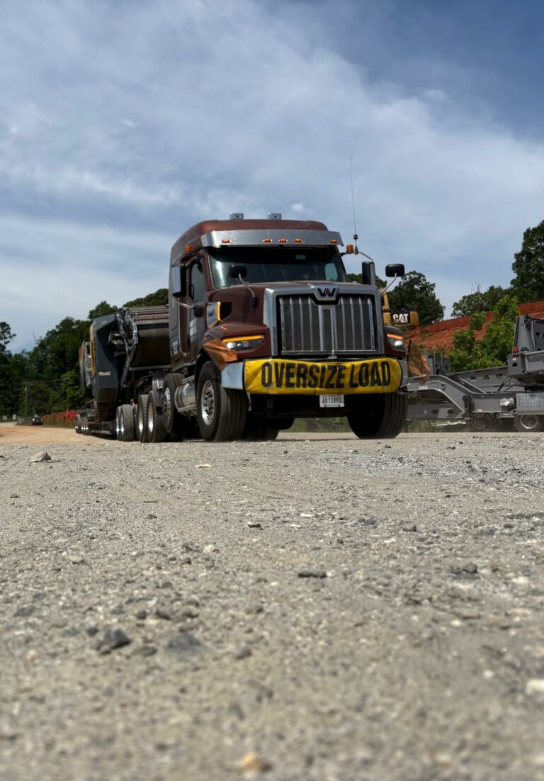 Semi truck with oversize load banner parked on gravel with lowboy trailer hauling a crusher