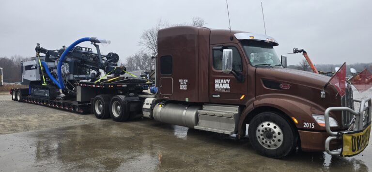 Heavy Haul Solutions semi tractor with lowboy trailer parked in yard, carrying industrial machinery