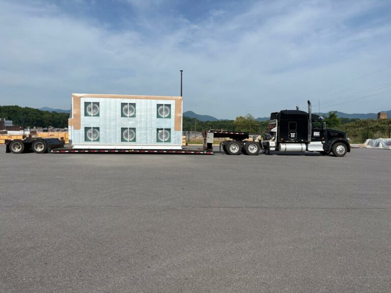 Semi tractor and flatbed trailer parked with large industrial ventilation units mounted on the lowboy trailer bed.