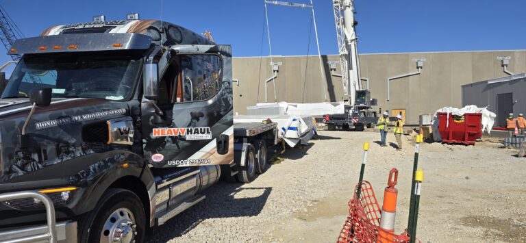 Heavy Haul Solutions semi truck parked at industrial site with crane and workers in background, construction equipment visible.