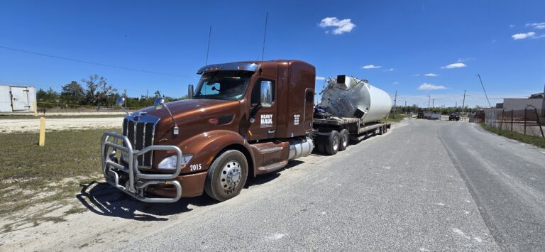 Heavy Haul Solutions semi tractor with brown cab hauling a tank on a step deck trailer.